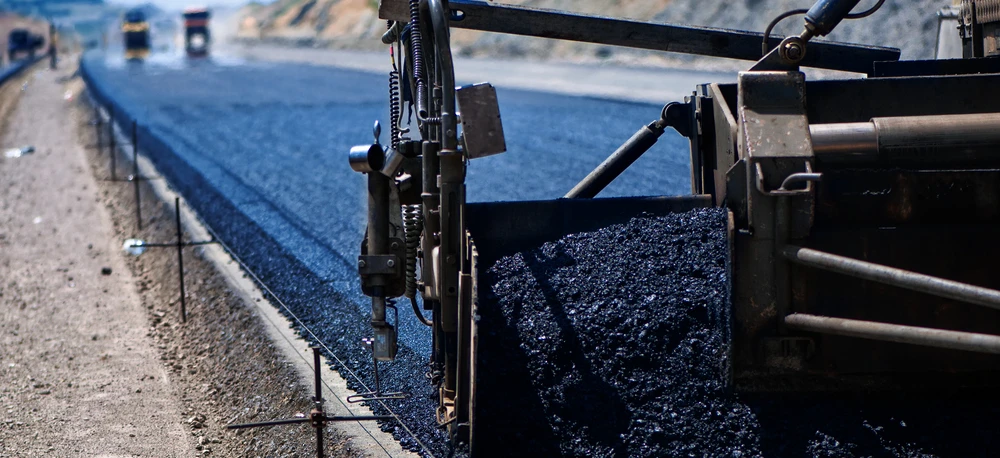 Duża maszyna układająca świeżą asfalt na nawierzchni drogi. Zasadniczy sprzęt ciężki do budowy materiałów takich jak beton i żwir na autostradzie.